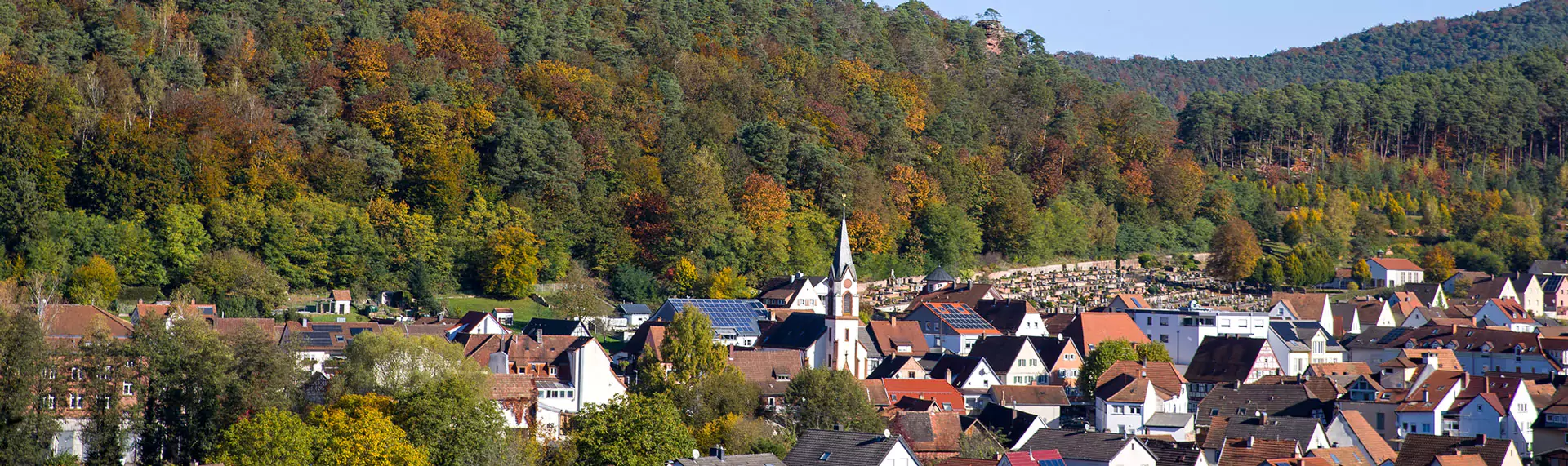 dahn Blick von oben auf die Stadt Dahn mit Friedhof und Kirche in Sonnenschein und Herbstwald
